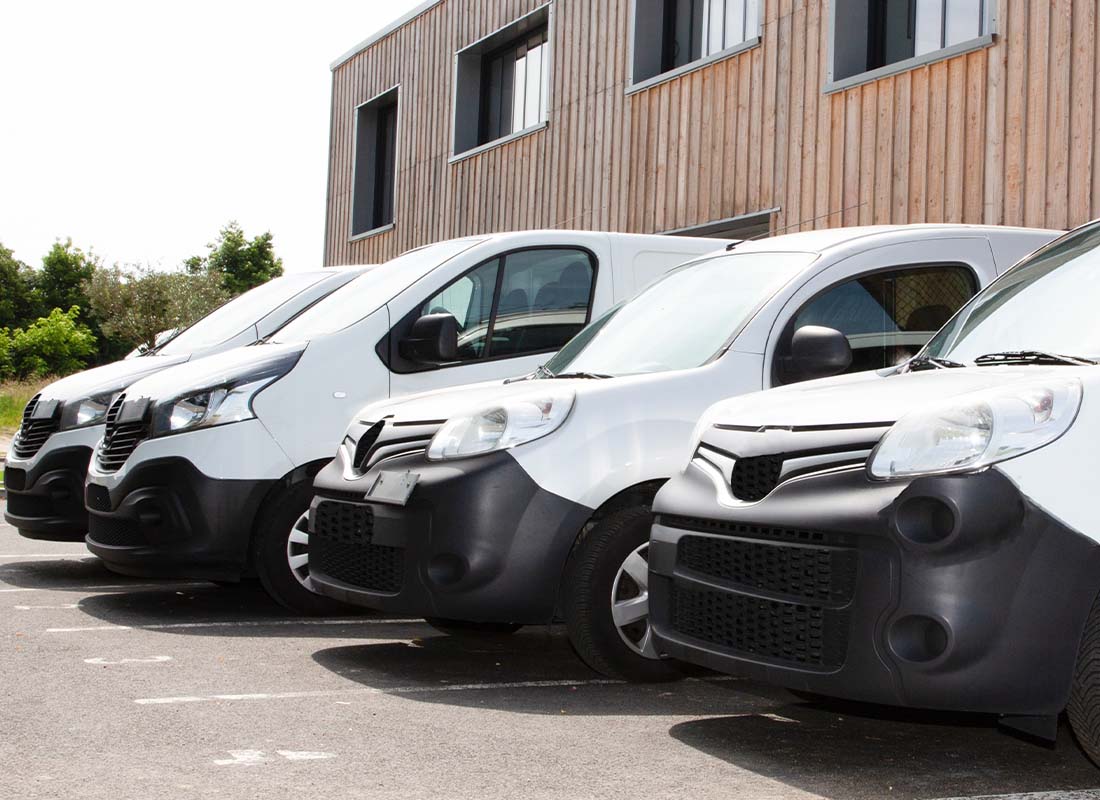 Fleet Insurance - Delivery Service of White Vans and Small Trucks Parked in a Row in Front of Factory Warehouse Distribution Plant on a Sunny Day