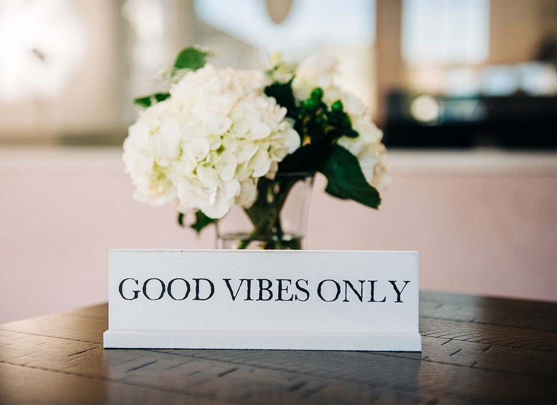 Read Our Reviews - Closeup View of a Good Vibes Only Sign In Front of a Flower Vase Sitting on Top of a Wooden Table Inside the Northwood Insurance Agency Office